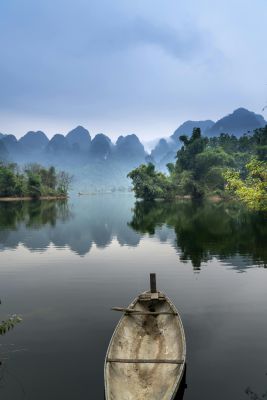 A tranquil river scene with a canoe, misty mountains, and lush greenery, perfect for nature lovers.